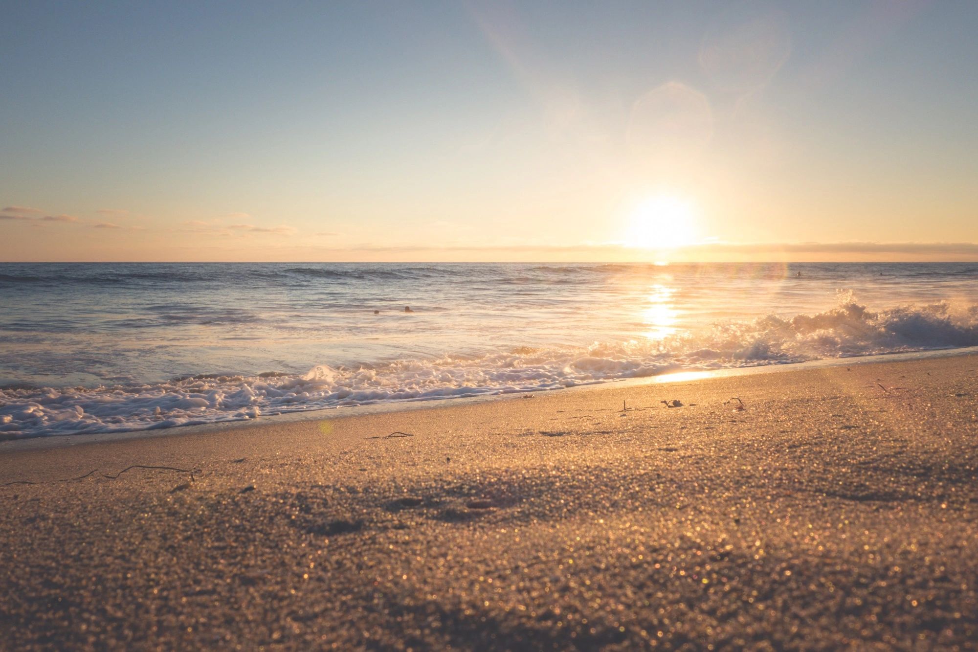 Sunset over a calm ocean with gentle waves on the sandy beach.