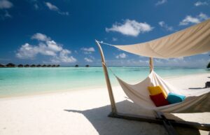 A hammock on a pristine beach with clear turquoise water and blue sky.