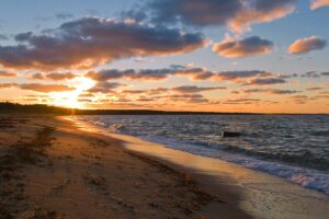 Sunset over a peaceful beach with gentle waves and scattered clouds.